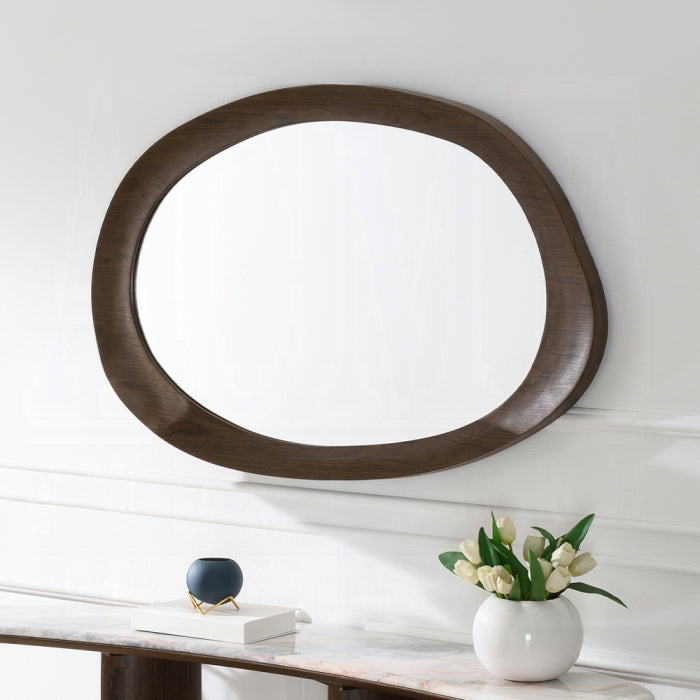 Round wooden mirror on a white wall with a vase of flowers on a table below.