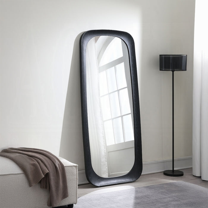 Large floor mirror with black frame in a room with a lamp and sofa.