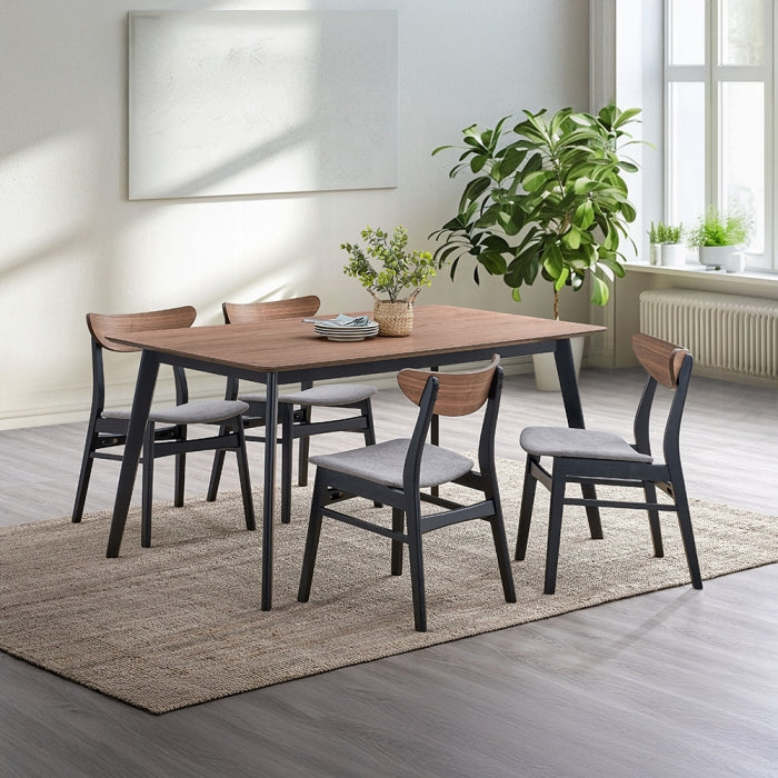 white background dinning table with 4 black legs base and a walnut colored finished as the table top surface staged in a dinning room setting with 4 matching chaise a few plants in the background and a carpet on the floor trying to match color tones with the light greys 