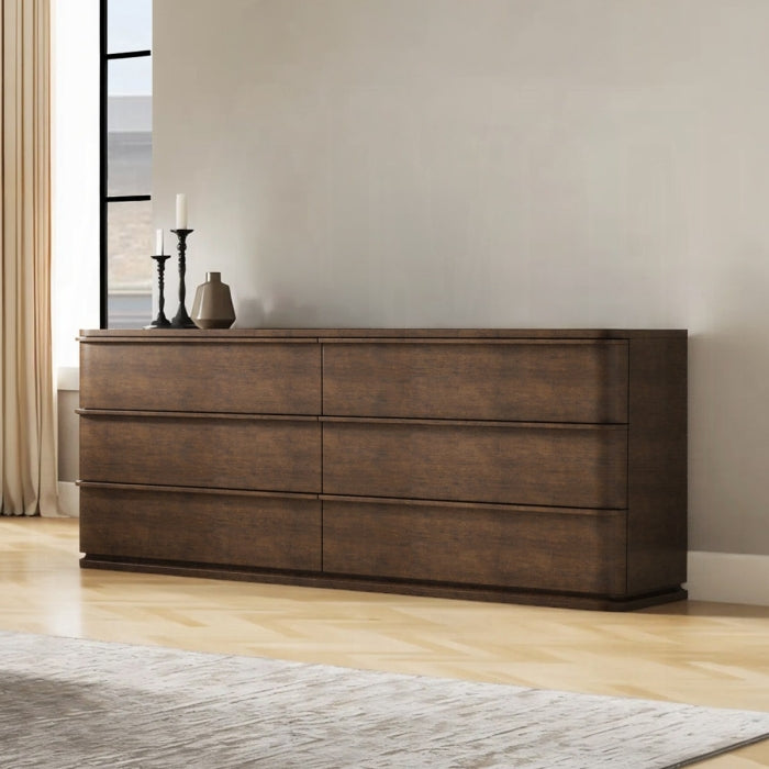 Wooden dresser with decorative items in a room with light-colored walls and wooden floor.