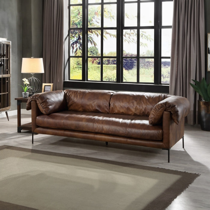 Brown leather sofa in a living room with large windows and decor elements.
